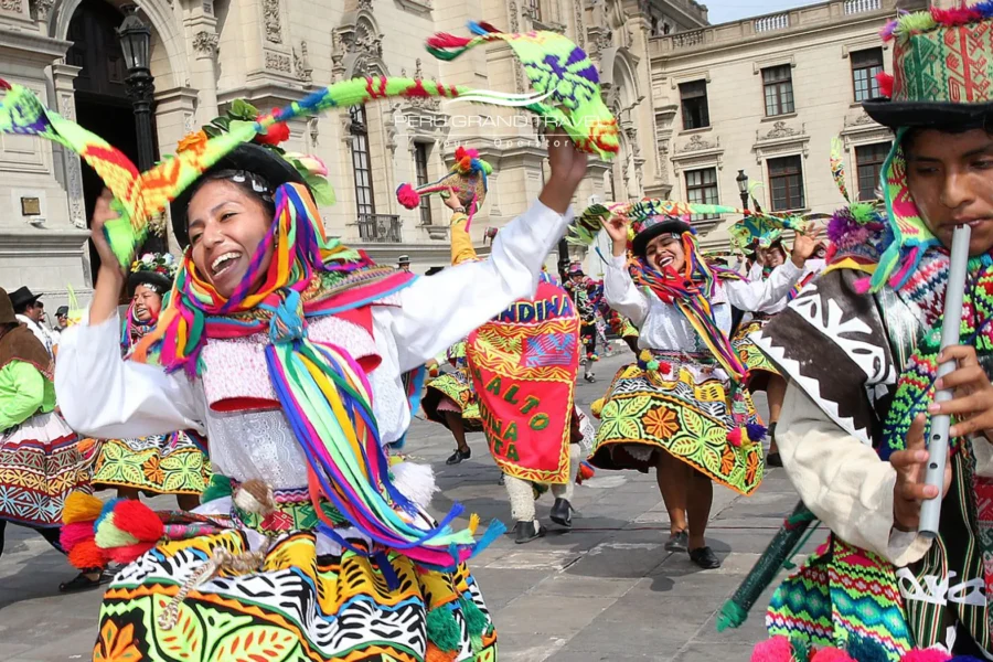 Dançarinos de comparsa com trajes andinos coloridos durante o Carnaval de Ayacucho, no Peru, apresentando danças folclóricas em uma praça colonial histórica.