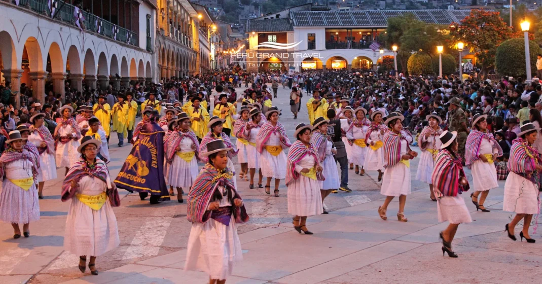 Desfile noturno de comparsa no Carnaval de Ayacucho, com mulheres usando polleras e mantas tradicionais dançando pelo centro histórico cercadas pela multidão.