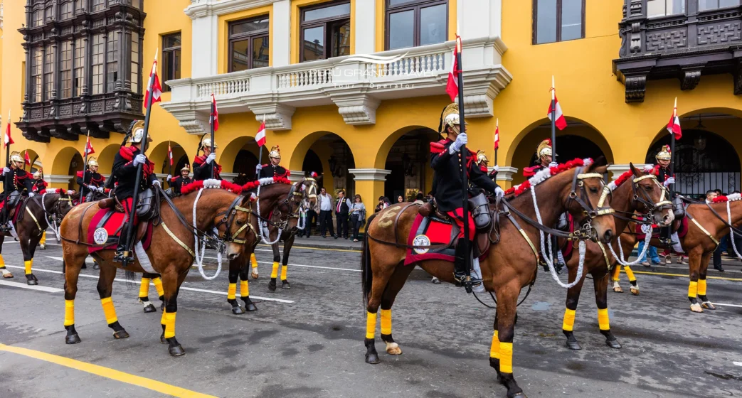 Guarda montada em um desfile cerimonial no Centro Histórico de Lima, com bandeiras do Peru e arquitetura colonial amarela ao fundo