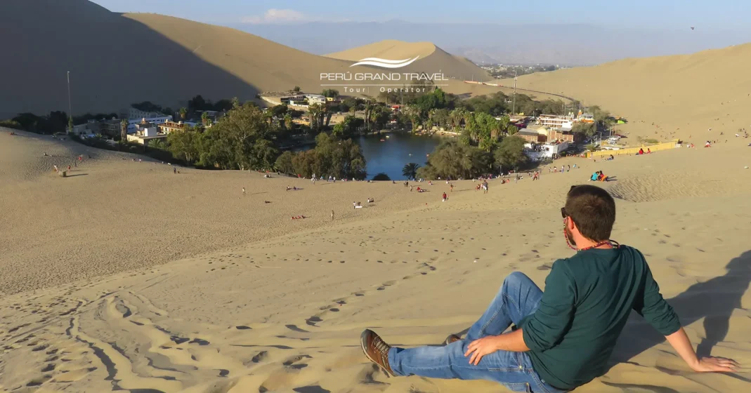 Oásis de Huacachina no verão, com dunas de areia dourada, sol intenso e turistas aproveitando atividades no deserto.