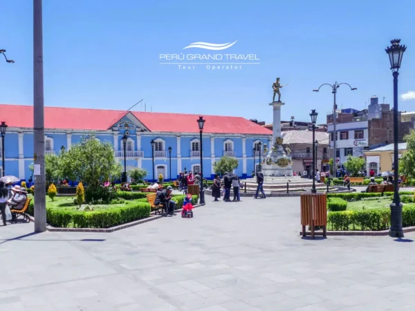 Parque Pino em Puno, no Peru, com jardins, bancos e o monumento central, cercada por edifícios coloniais sob um céu andino azul e limpo.