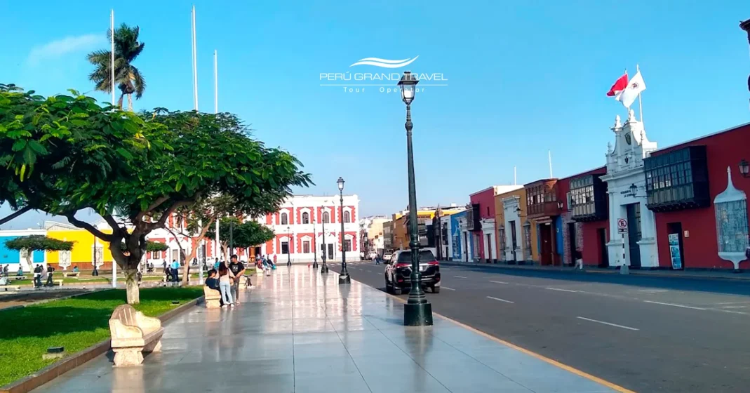 Rua histórica em Trujillo, Peru, com edifícios coloniais coloridos, palmeiras e pedestres caminhando pelo centro da cidade em um dia ensolarado