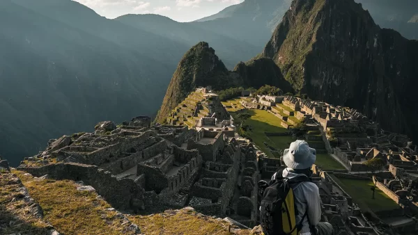 turista sentado observando Machu Picchu suas construções e espaço inca, cercado por montanhas e um céu azul claro