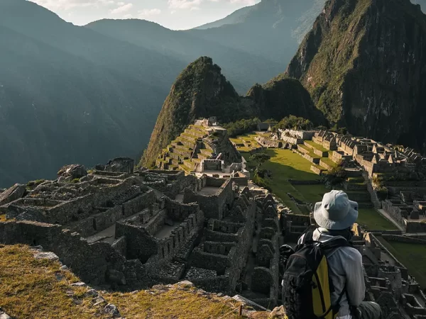 turista sentado observando Machu Picchu suas construções e espaço inca, cercado por montanhas e um céu azul claro